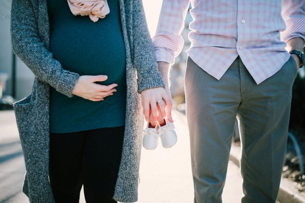 Expectant parents holding baby shoes outdoors