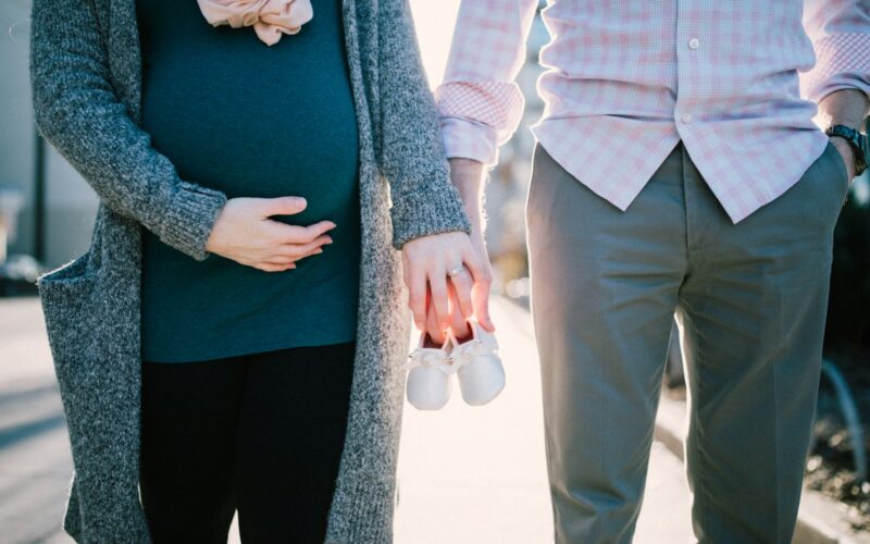 Expectant parents holding baby shoes outdoors